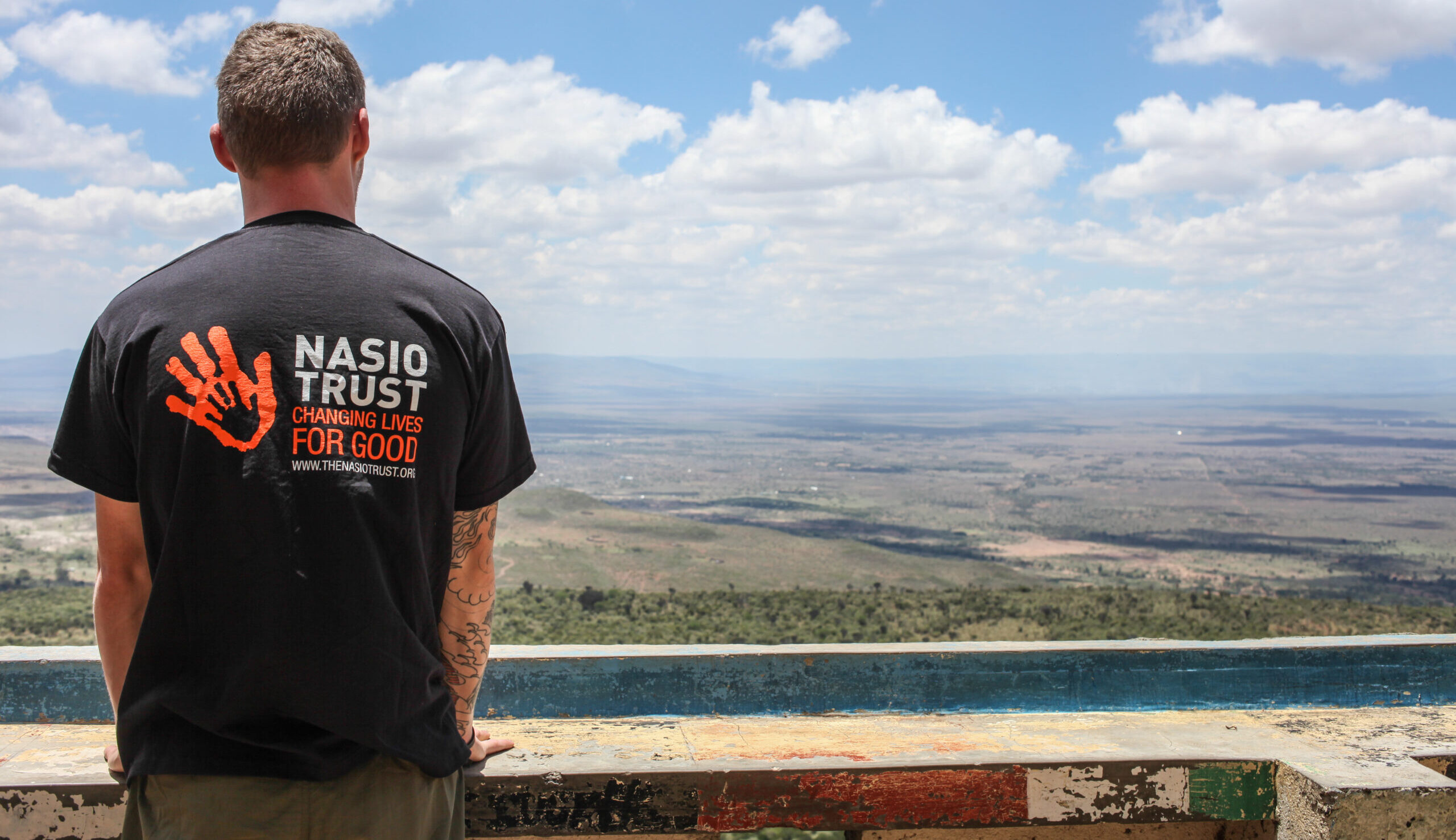 Man in Nasio Trust T-Shirt looking out from a viewpoint